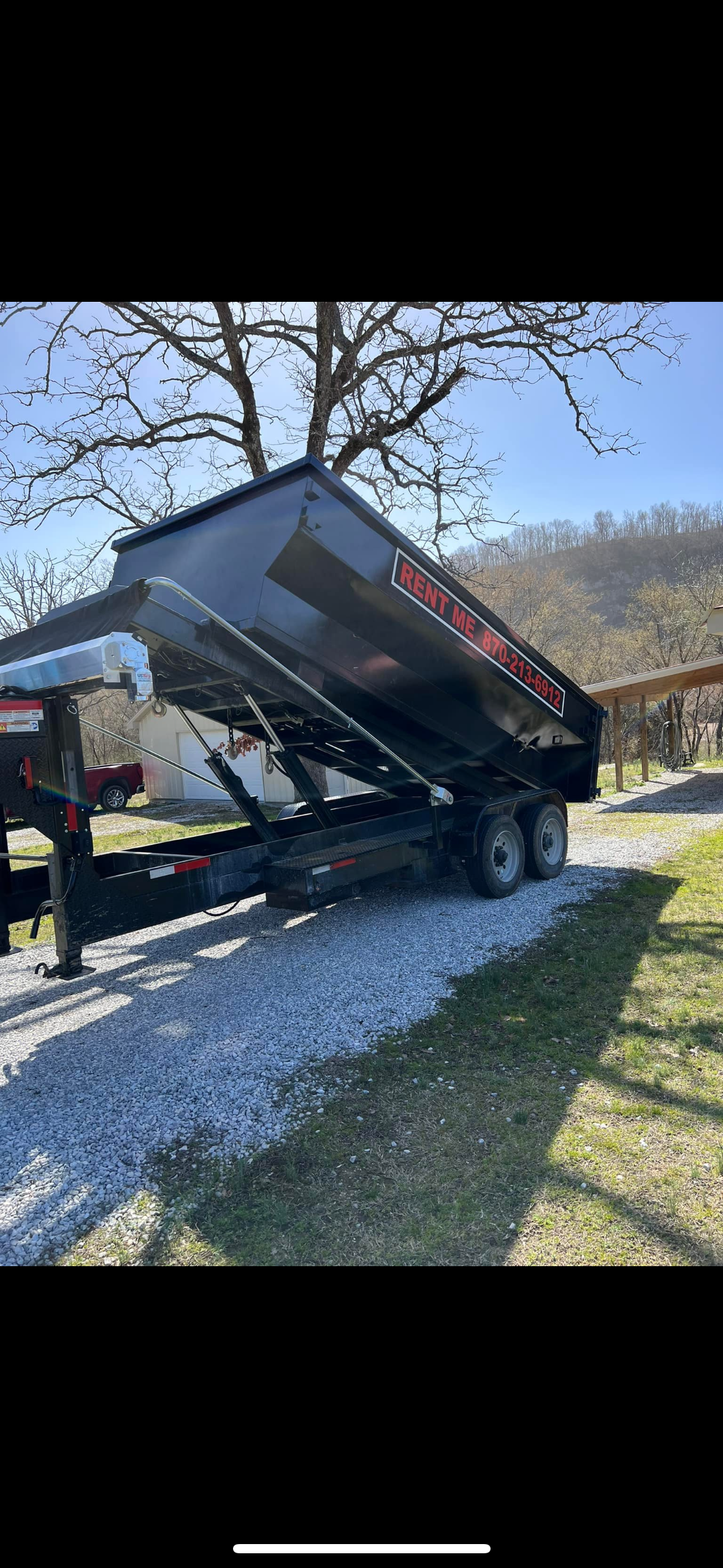 An exterior shot of a green rolling trash bin with a black slatted lid, situated in a concrete courtyard between light-col...